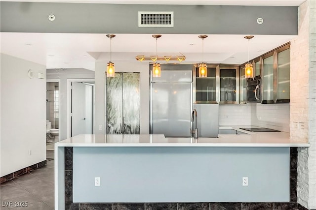 kitchen featuring decorative light fixtures, a peninsula, visible vents, light countertops, and glass insert cabinets