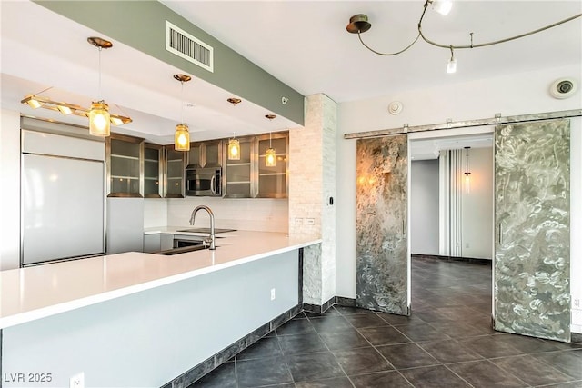 kitchen featuring stainless steel microwave, visible vents, a barn door, glass insert cabinets, and paneled fridge