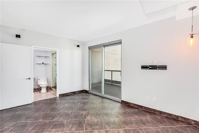 unfurnished bedroom with dark tile patterned floors, a closet, connected bathroom, and baseboards