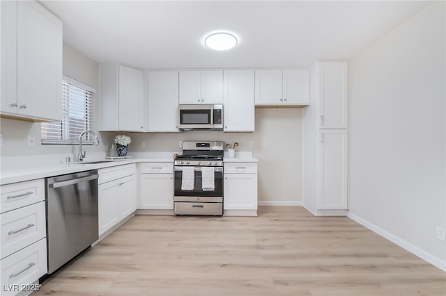 kitchen with stainless steel appliances, light countertops, white cabinets, a sink, and baseboards