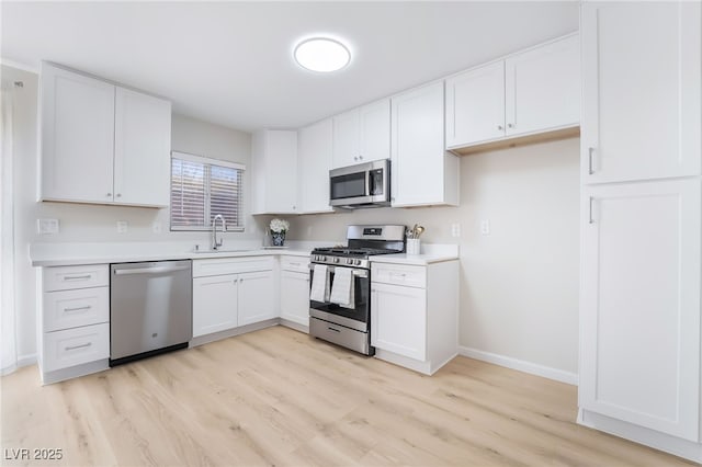 kitchen with light wood-style flooring, stainless steel appliances, a sink, white cabinetry, and light countertops