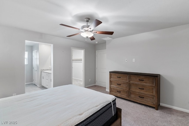 bedroom featuring ensuite bathroom, light colored carpet, visible vents, baseboards, and a walk in closet