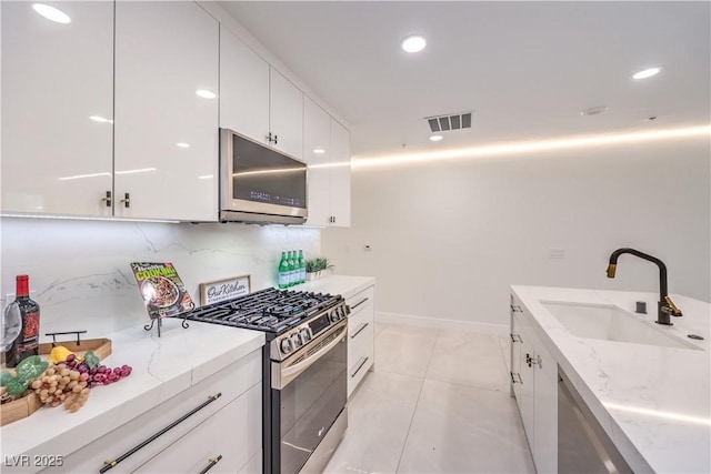 kitchen featuring white cabinets, modern cabinets, light stone counters, appliances with stainless steel finishes, and a sink