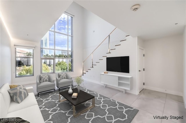 living room with a towering ceiling, stairway, and baseboards