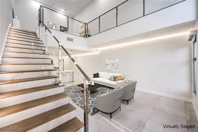 stairs featuring baseboards, visible vents, and a high ceiling