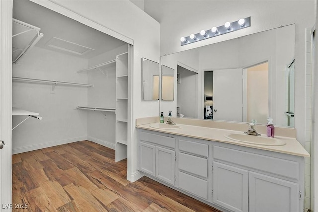 bathroom with a sink, double vanity, wood finished floors, and a walk in closet