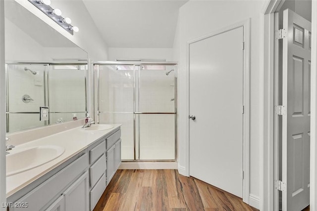 full bathroom featuring double vanity, wood finished floors, a sink, and a shower stall