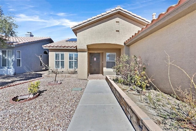 view of exterior entry with a tiled roof and stucco siding