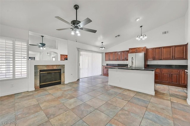 kitchen with open floor plan, freestanding refrigerator, dark countertops, a tiled fireplace, and pendant lighting