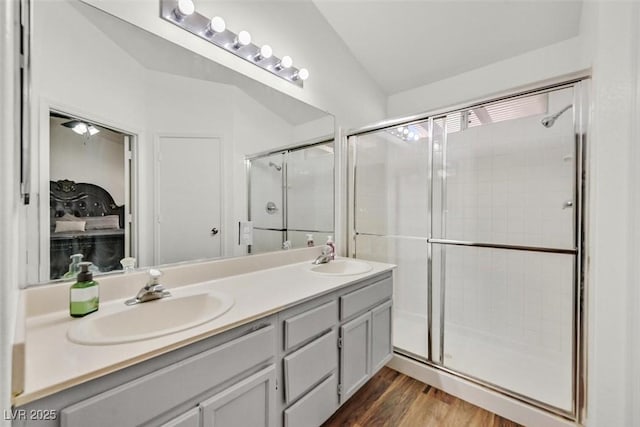 bathroom with a stall shower, double vanity, a sink, and wood finished floors