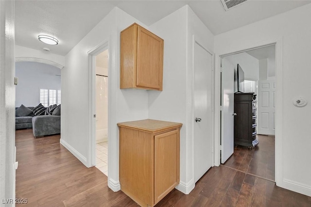 hall featuring arched walkways, dark wood finished floors, visible vents, and baseboards