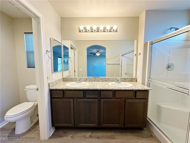 full bathroom with a sink, a shower stall, toilet, and double vanity