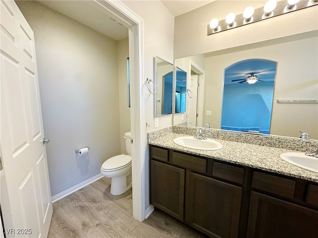 full bath featuring toilet, double vanity, a sink, and wood finished floors