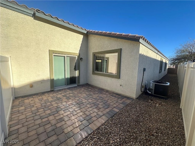 rear view of property with a patio, a fenced backyard, a tiled roof, central AC, and stucco siding