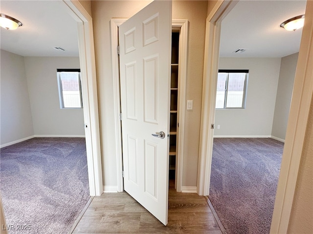 corridor with baseboards, light wood finished floors, visible vents, and light colored carpet