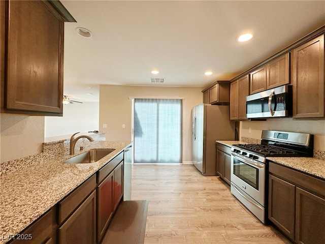 kitchen with visible vents, light stone countertops, stainless steel appliances, light wood-type flooring, and a sink