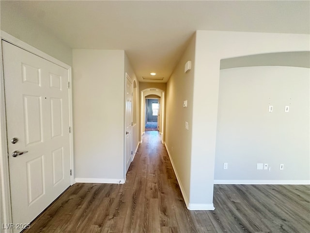 hallway featuring dark wood-style floors, arched walkways, and baseboards