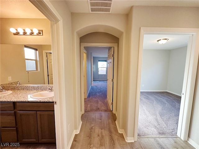 corridor featuring light wood finished floors, visible vents, a sink, and light colored carpet