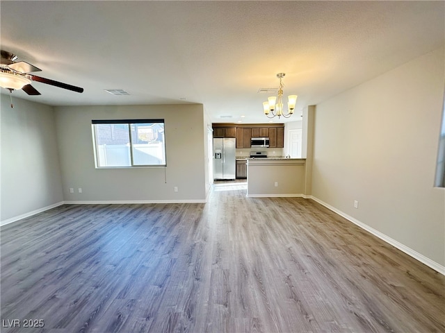 unfurnished living room featuring light wood-style flooring, visible vents, baseboards, and ceiling fan with notable chandelier