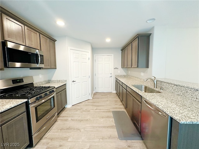 kitchen with appliances with stainless steel finishes, light stone counters, light wood-type flooring, a sink, and recessed lighting