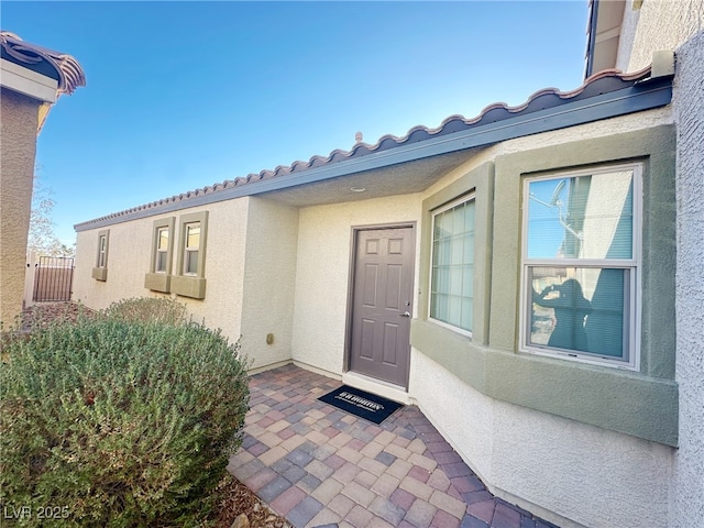 view of exterior entry with a patio area, a tiled roof, and stucco siding