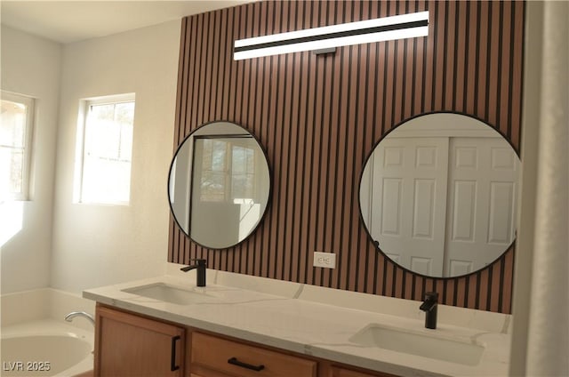 bathroom with double vanity, wallpapered walls, a garden tub, and a sink