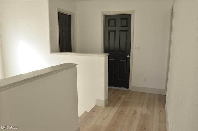 hall with light wood-type flooring, an upstairs landing, and baseboards