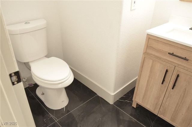 bathroom featuring marble finish floor, baseboards, vanity, and toilet