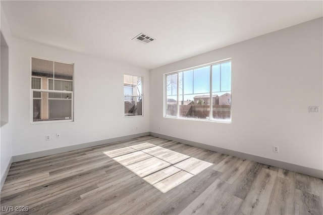 spare room with wood finished floors, visible vents, and baseboards