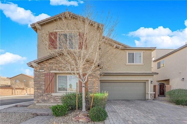 traditional-style house with stone siding, decorative driveway, an attached garage, and stucco siding