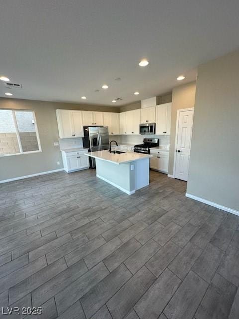 kitchen with stainless steel appliances, light countertops, a kitchen island with sink, white cabinetry, and a sink