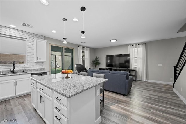 kitchen featuring a kitchen island, visible vents, a sink, open floor plan, and white cabinetry