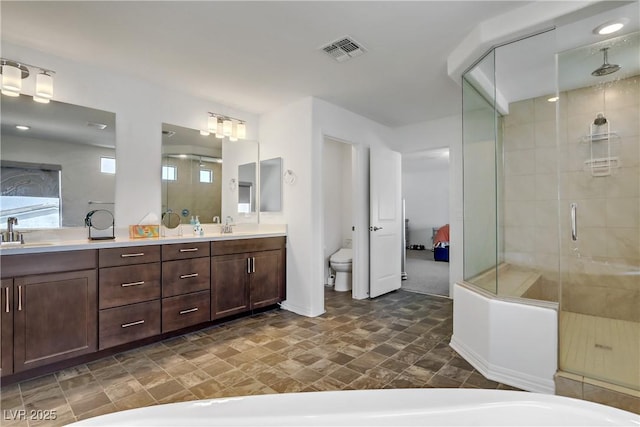 bathroom featuring double vanity, visible vents, toilet, a sink, and a shower stall