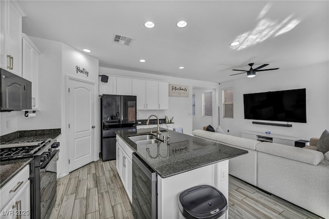 kitchen with visible vents, a kitchen island with sink, black appliances, white cabinetry, and a sink