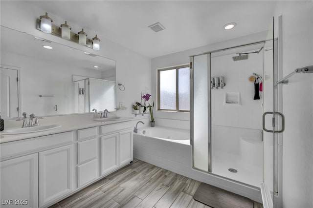 bathroom featuring a stall shower, wood finished floors, a sink, and double vanity