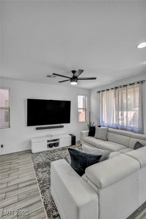 living room with light wood finished floors, visible vents, and a ceiling fan