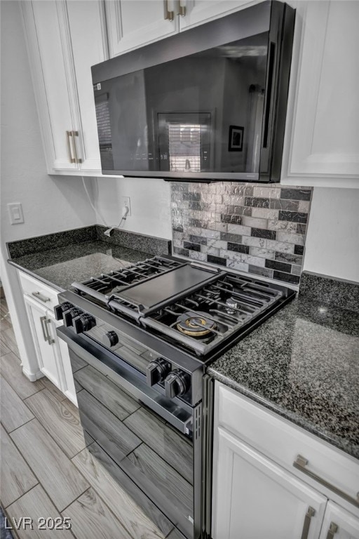 kitchen featuring range with two ovens, dark stone counters, white cabinets, and tasteful backsplash