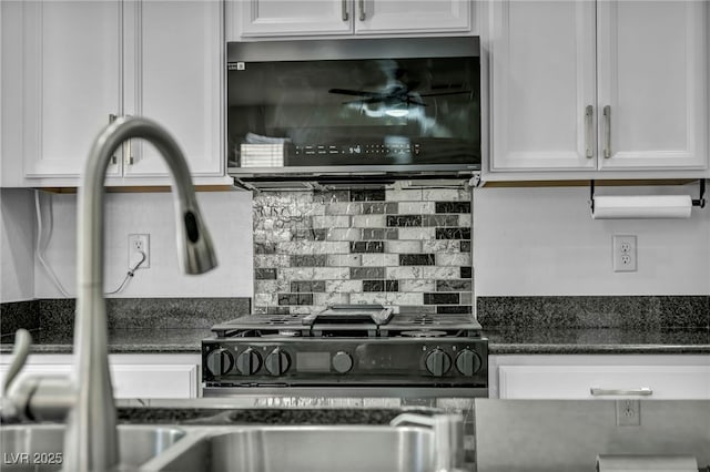 kitchen featuring stainless steel microwave, white cabinets, backsplash, and dark stone counters