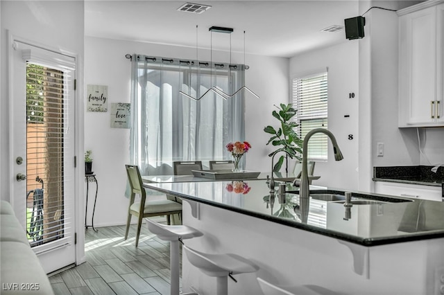 kitchen with visible vents, a kitchen bar, white cabinetry, and a sink