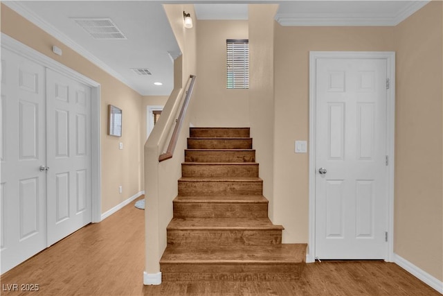 stairway with ornamental molding, visible vents, baseboards, and wood finished floors