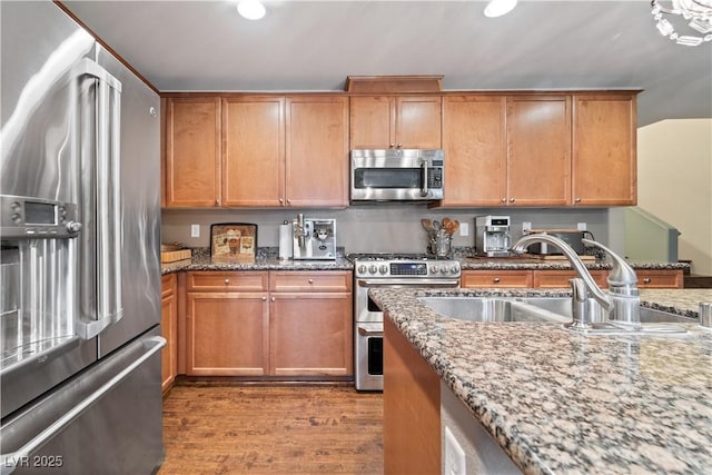 kitchen featuring light stone counters, wood finished floors, a sink, stainless steel appliances, and brown cabinets