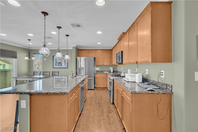 kitchen with visible vents, light wood finished floors, dark stone counters, a kitchen island with sink, and appliances with stainless steel finishes