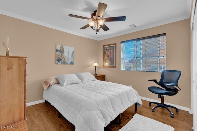 bedroom with visible vents, baseboards, wood finished floors, and crown molding