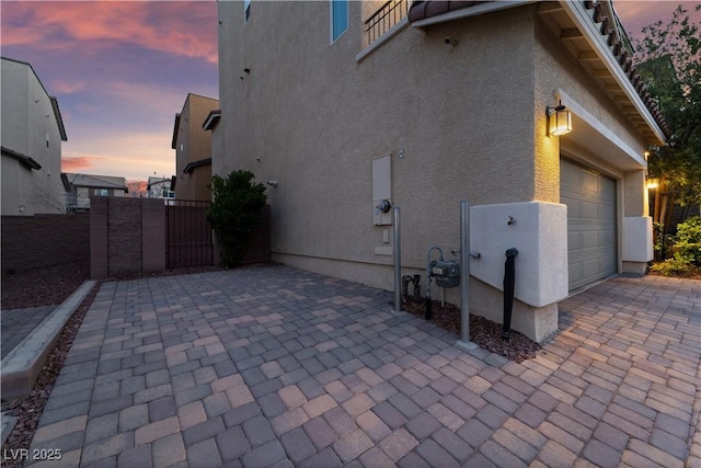 property exterior at dusk featuring stucco siding, fence, and decorative driveway
