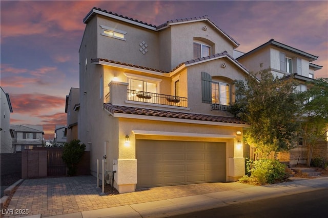 mediterranean / spanish home featuring a tiled roof, stucco siding, decorative driveway, a balcony, and an attached garage