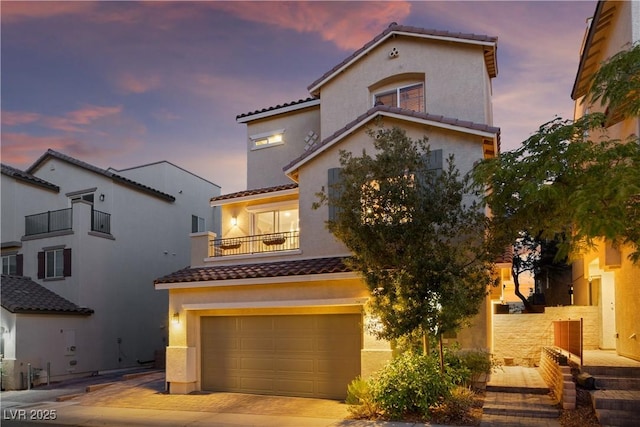 mediterranean / spanish-style home with stucco siding, decorative driveway, an attached garage, a balcony, and a tiled roof