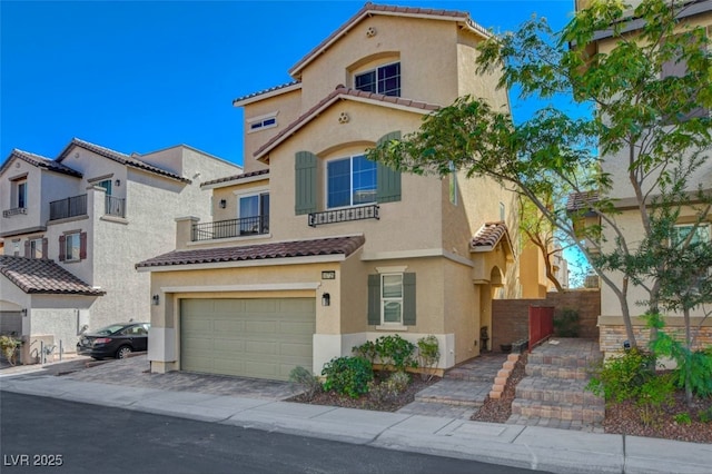 mediterranean / spanish house with an attached garage, a tiled roof, stucco siding, and decorative driveway