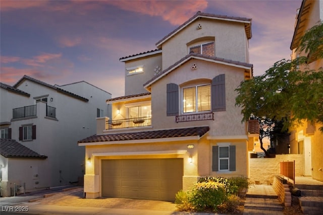 mediterranean / spanish house featuring a tiled roof, driveway, stucco siding, and a balcony