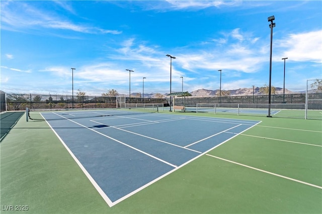 view of tennis court with community basketball court, a mountain view, and fence