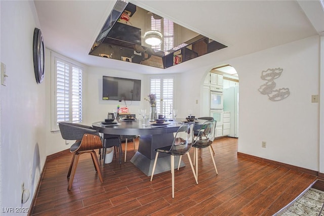 dining space with dark wood-style floors, baseboards, and arched walkways